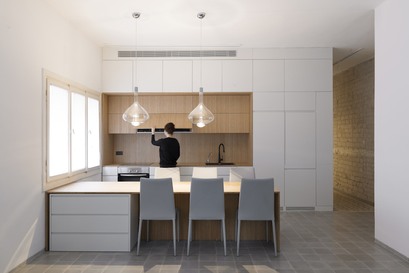 The kitchen occupies a corner space and receives light through the windows and from the pendants